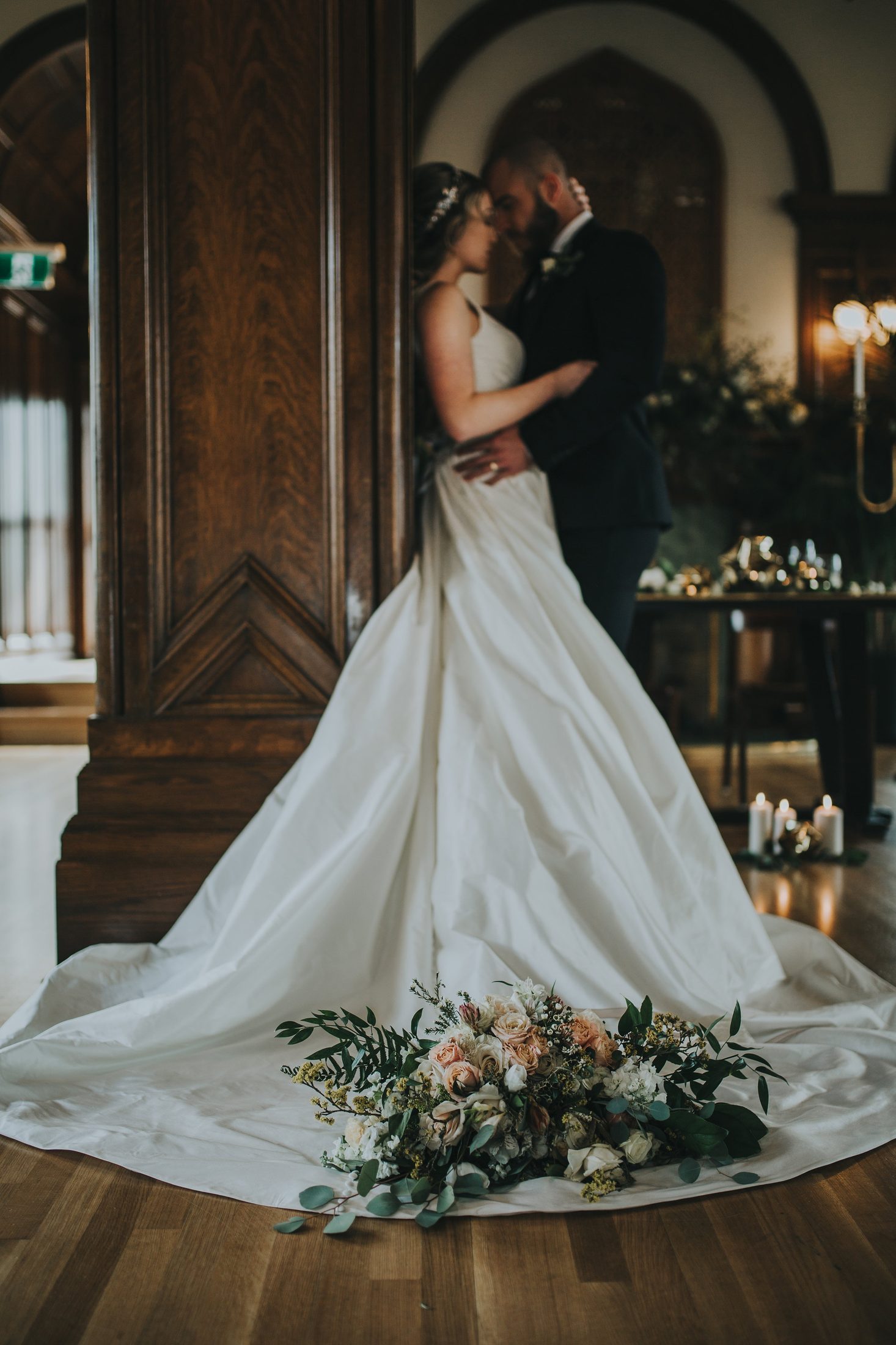 Bouquet and gown detail in the foreground, the couple softly framed behind.